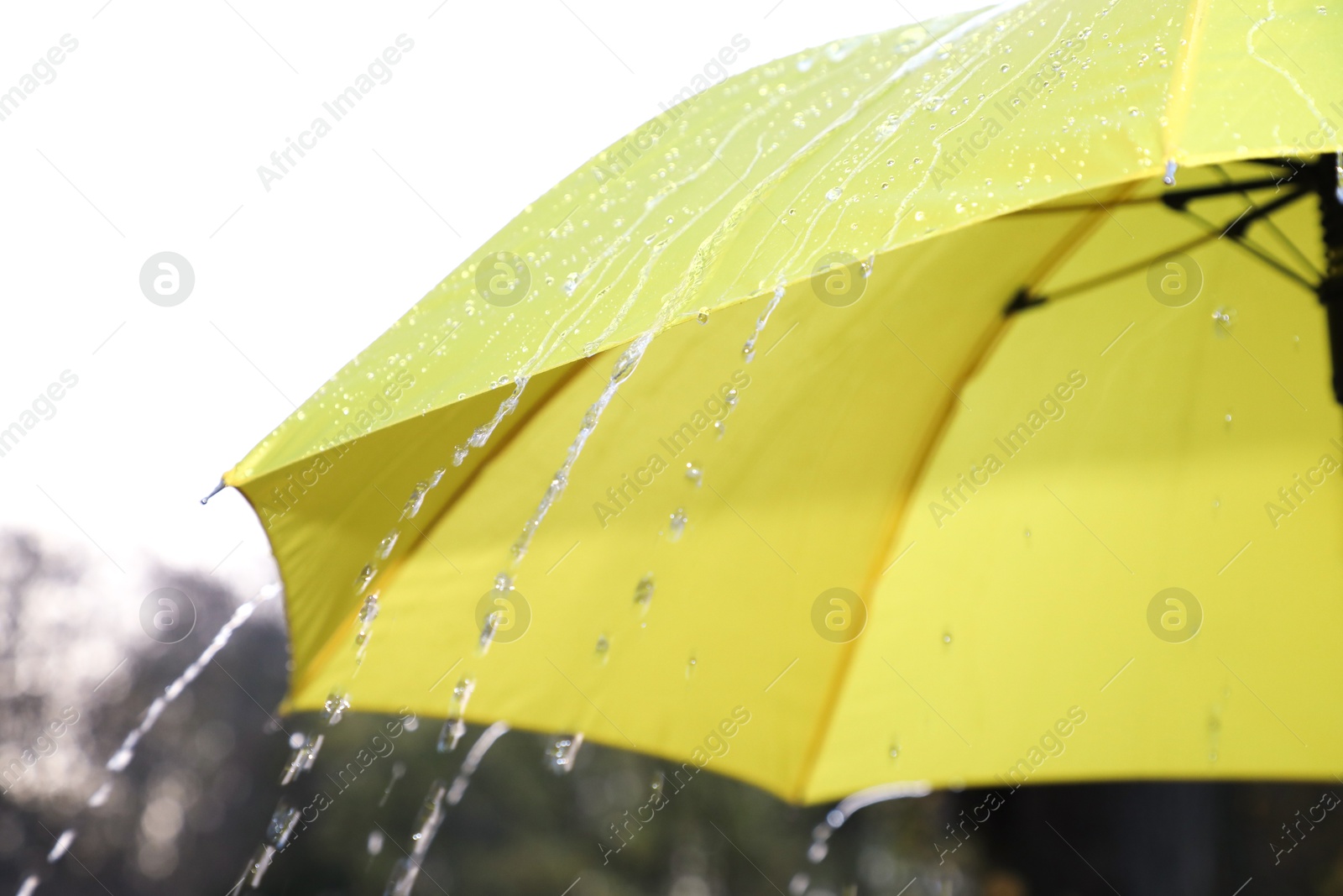 Photo of Open yellow umbrella under pouring rain outdoors, closeup