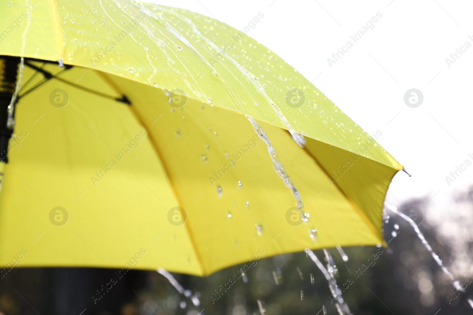 Photo of Open yellow umbrella under pouring rain outdoors, closeup