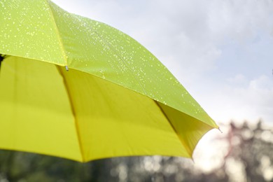 Photo of Open yellow umbrella under pouring rain outdoors, closeup. Space for text