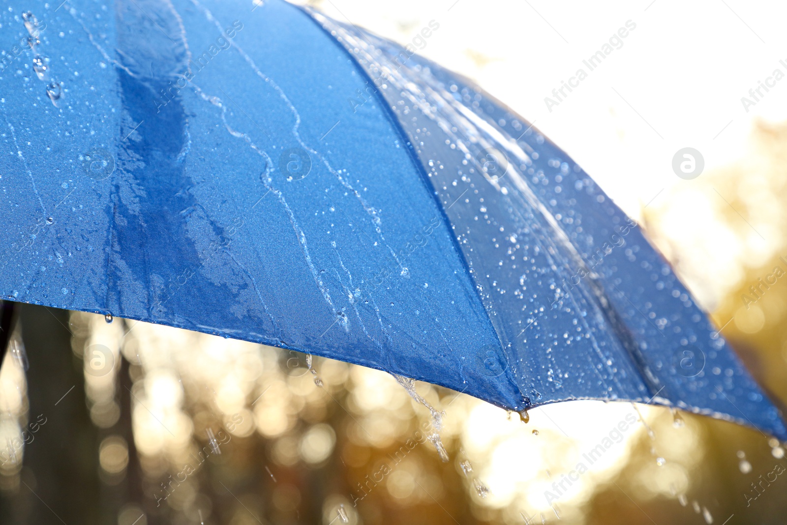 Photo of Open blue umbrella under pouring rain outdoors, closeup