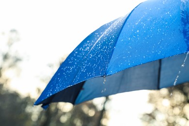 Photo of Open blue umbrella under pouring rain outdoors, closeup