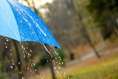 Photo of Open blue umbrella under pouring rain outdoors, closeup. Space for text