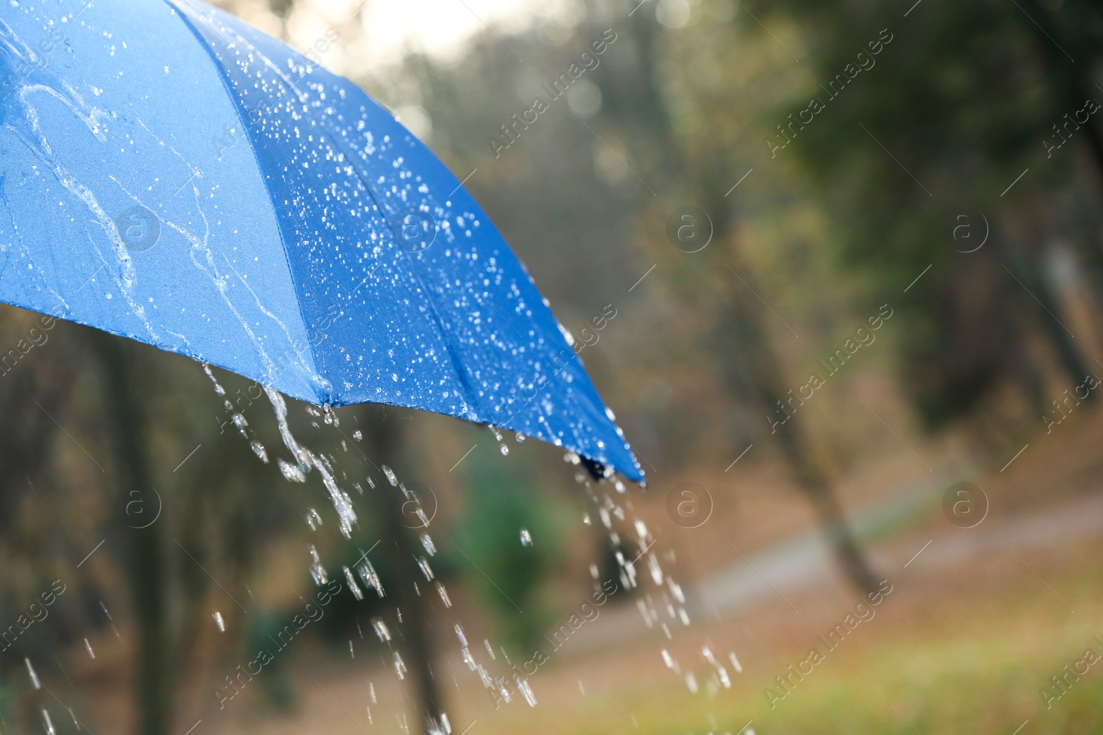 Photo of Open blue umbrella under pouring rain outdoors, closeup. Space for text