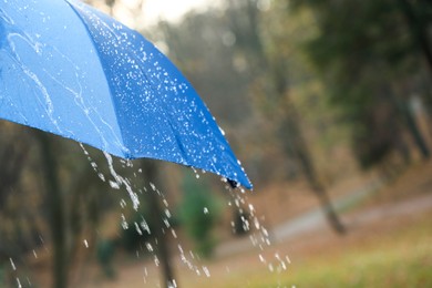 Photo of Open blue umbrella under pouring rain outdoors, closeup. Space for text