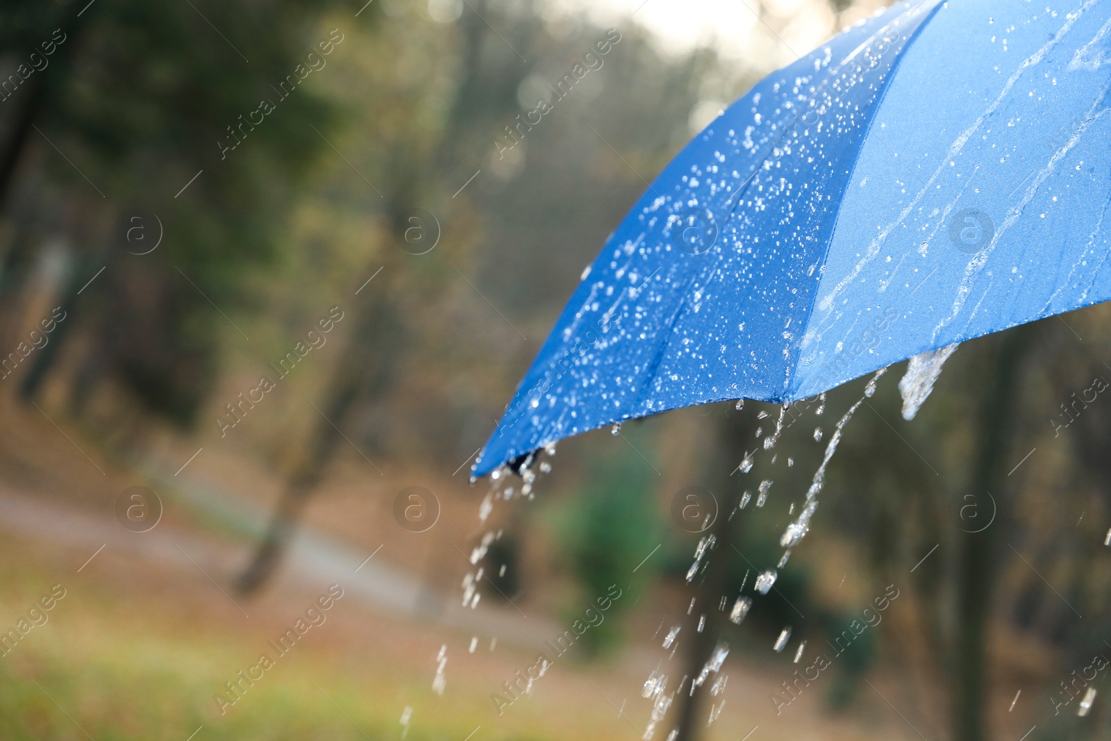 Photo of Open blue umbrella under pouring rain outdoors, closeup. Space for text