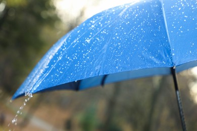 Photo of Open blue umbrella under pouring rain outdoors, closeup