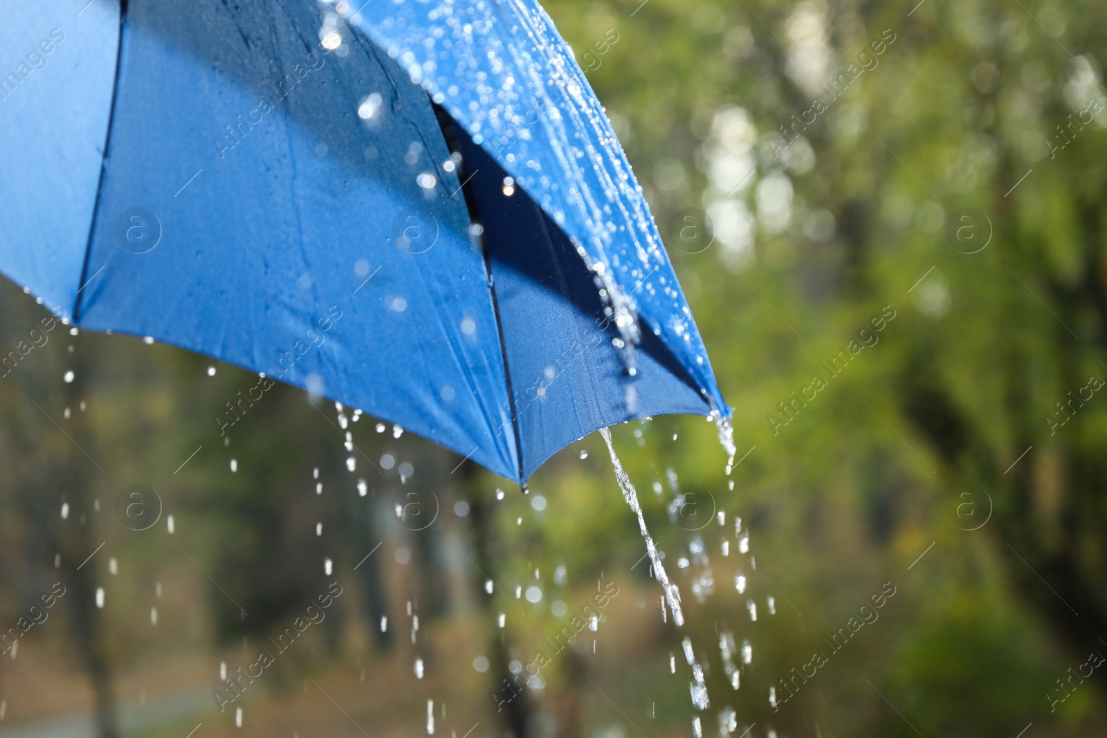 Photo of Open blue umbrella under pouring rain outdoors, closeup