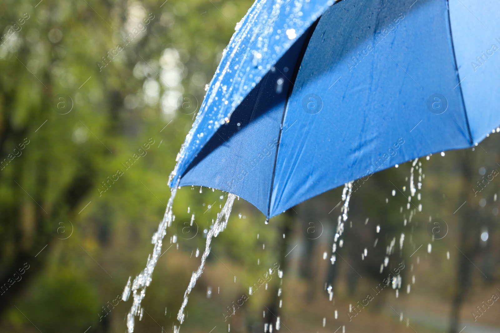 Photo of Open blue umbrella under pouring rain outdoors, closeup