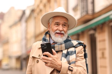 Photo of Stylish senior man with smartphone on city street