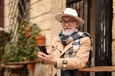 Stylish senior man with smartphone in outdoor bar