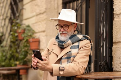 Photo of Stylish senior man with smartphone in outdoor bar