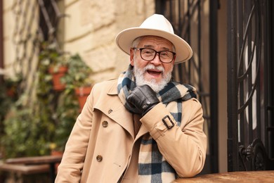 Photo of Stylish senior man with hat and scarf in outdoor bar