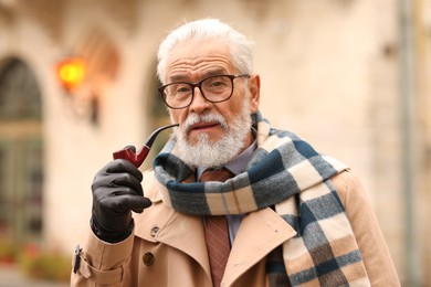 Photo of Stylish senior man with tobacco pipe on city street