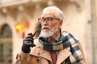 Photo of Stylish senior man with tobacco pipe on city street