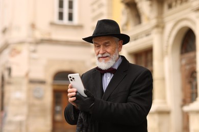 Photo of Elegant senior man with smartphone on city street