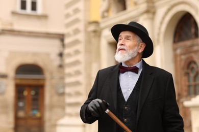 Photo of Elegant senior man with walking cane on city street. Space for text