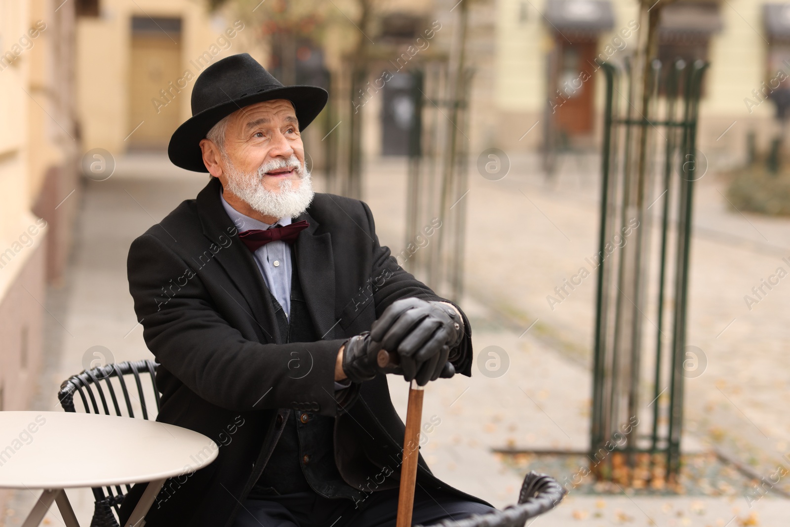 Photo of Bearded senior man with walking cane in outdoor cafe. Space for text