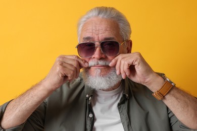 Photo of Stylish senior man in sunglasses on orange background