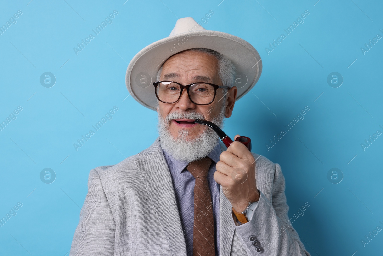 Photo of Stylish senior man with tobacco pipe on light blue background