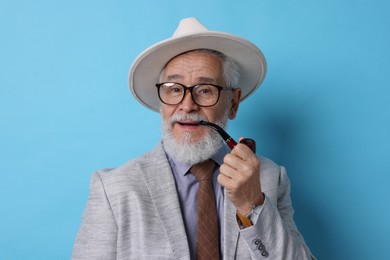 Photo of Stylish senior man with tobacco pipe on light blue background