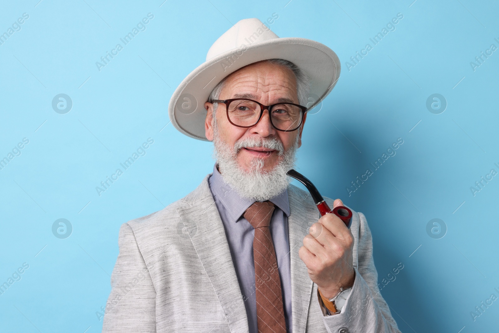 Photo of Stylish senior man with tobacco pipe on light blue background