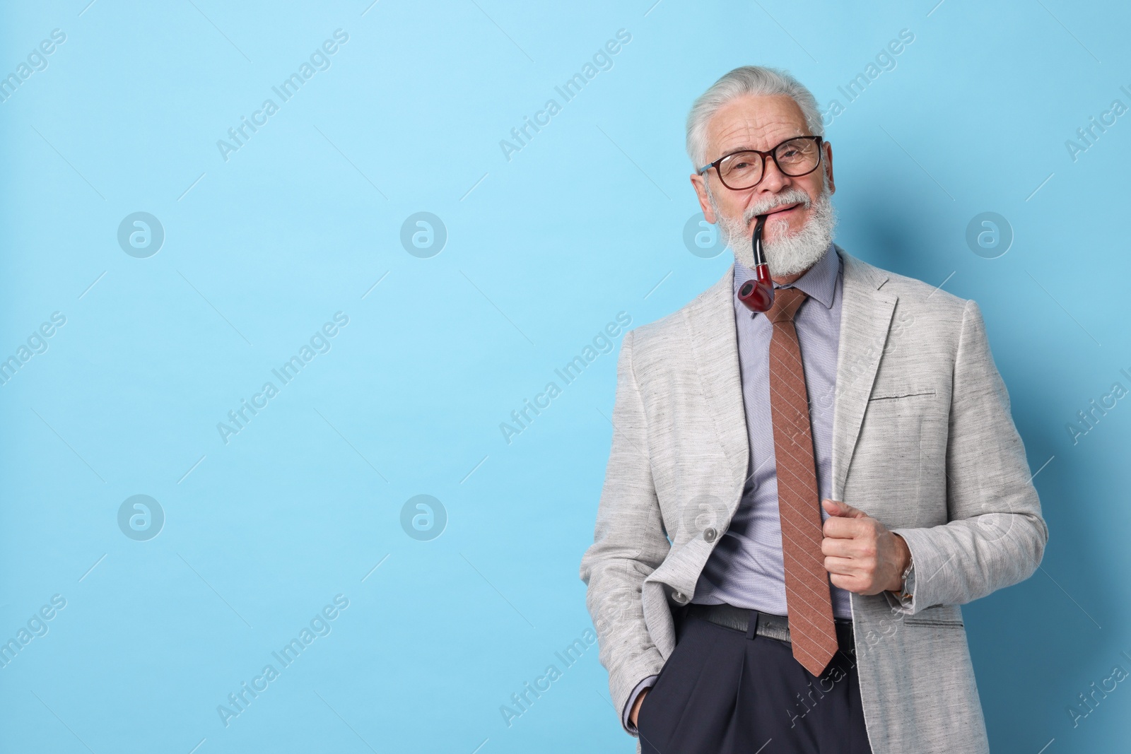 Photo of Confident senior man with tobacco pipe on light blue background. Space for text