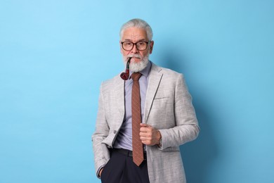 Photo of Confident senior man with tobacco pipe on light blue background