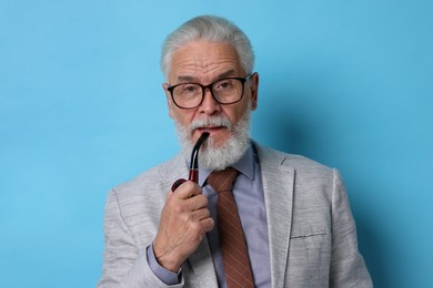 Photo of Confident senior man with tobacco pipe on light blue background