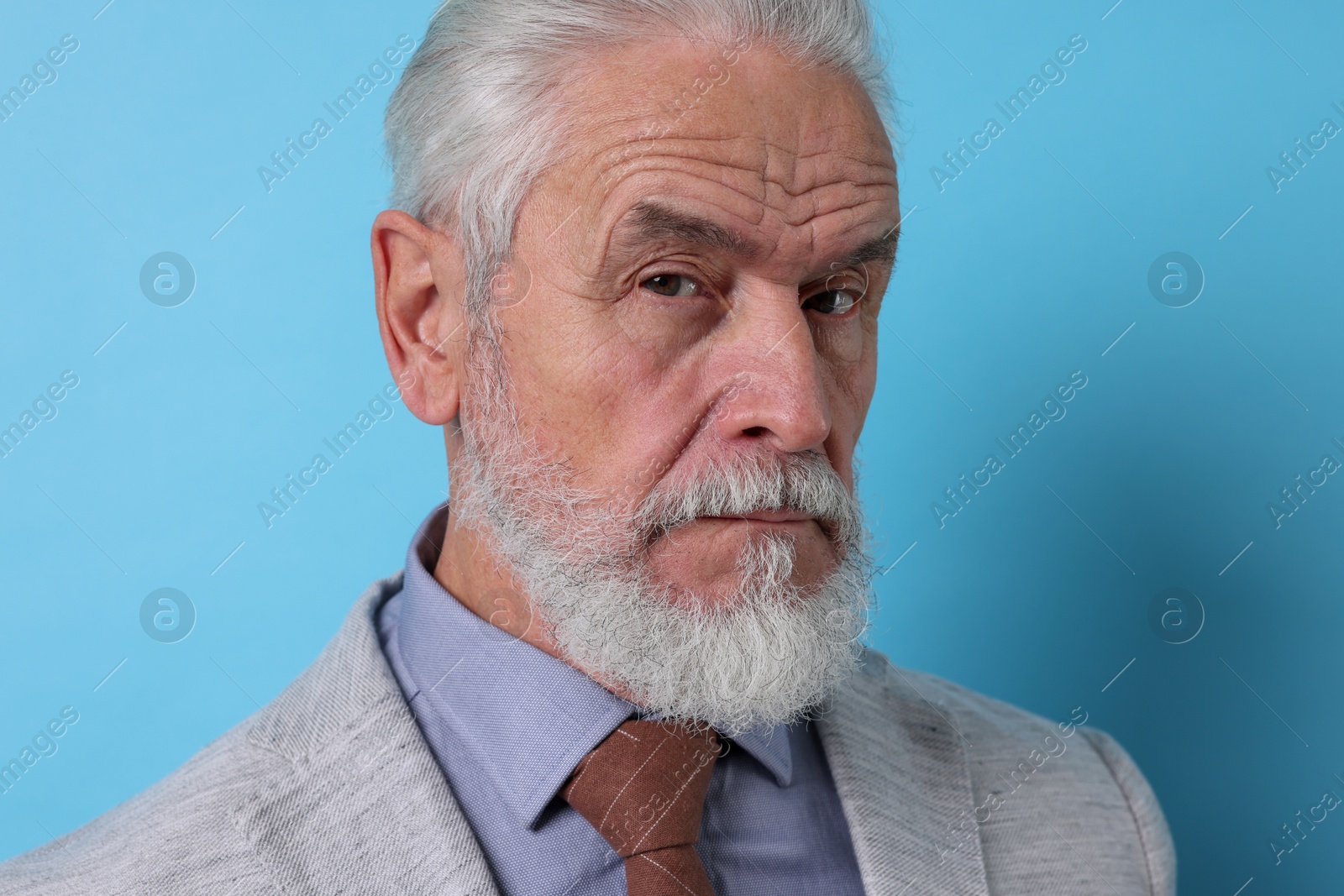 Photo of Portrait of serious senior man with silver beard on light blue background