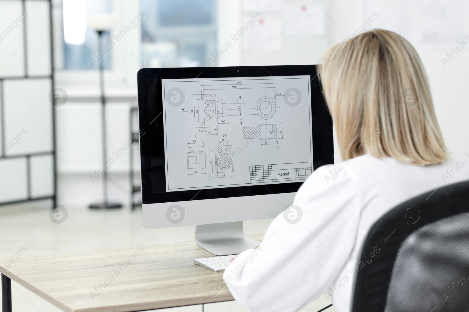 Photo of Technician making digital engineering drawing on computer at desk in office, back view