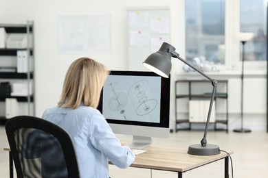 Photo of Technician making digital engineering drawing on computer at desk in office, back view