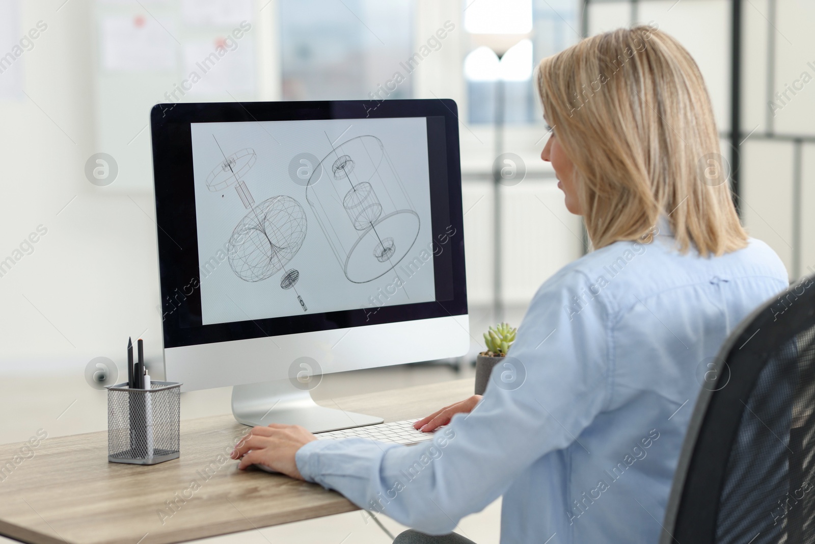 Photo of Technician making digital engineering drawing on computer at desk in office, back view