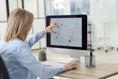 Photo of Technician making digital engineering drawing on computer at desk in office, back view