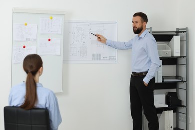 Photo of Man making presentation with engineering drawings to his colleagues in office