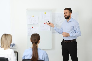 Photo of Man making presentation with engineering drawings to his colleagues in office