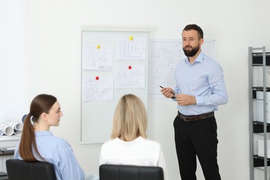 Photo of Man making presentation with engineering drawings to his colleagues in office