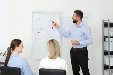 Photo of Man making presentation with engineering drawings to his colleagues in office