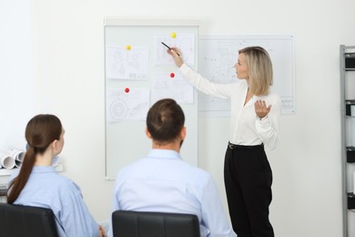 Photo of Woman making presentation with engineering drawings to her colleagues in office