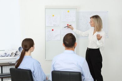 Photo of Woman making presentation with engineering drawings to her colleagues in office