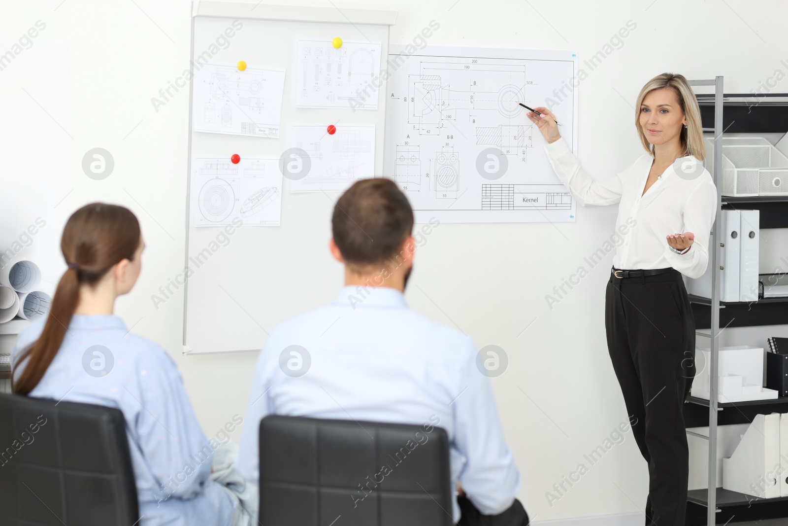 Photo of Woman making presentation with engineering drawings to her colleagues in office