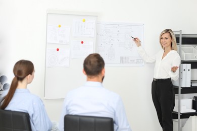 Photo of Woman making presentation with engineering drawings to her colleagues in office