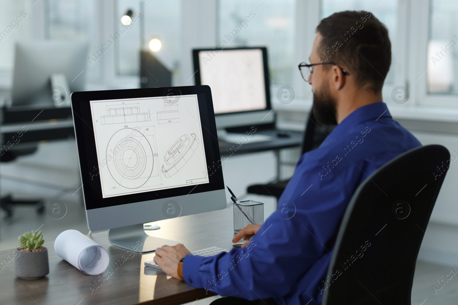 Photo of Technician making digital engineering drawing on computer at desk in office, back view