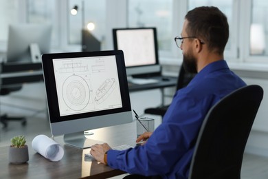 Photo of Technician making digital engineering drawing on computer at desk in office, back view