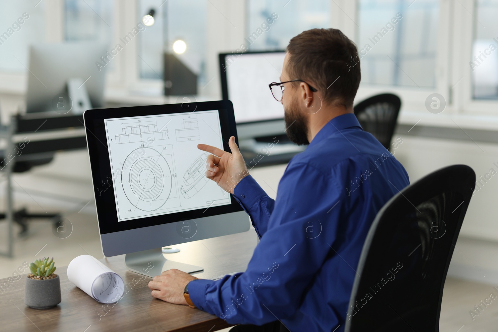 Photo of Technician making digital engineering drawing on computer at desk in office, back view