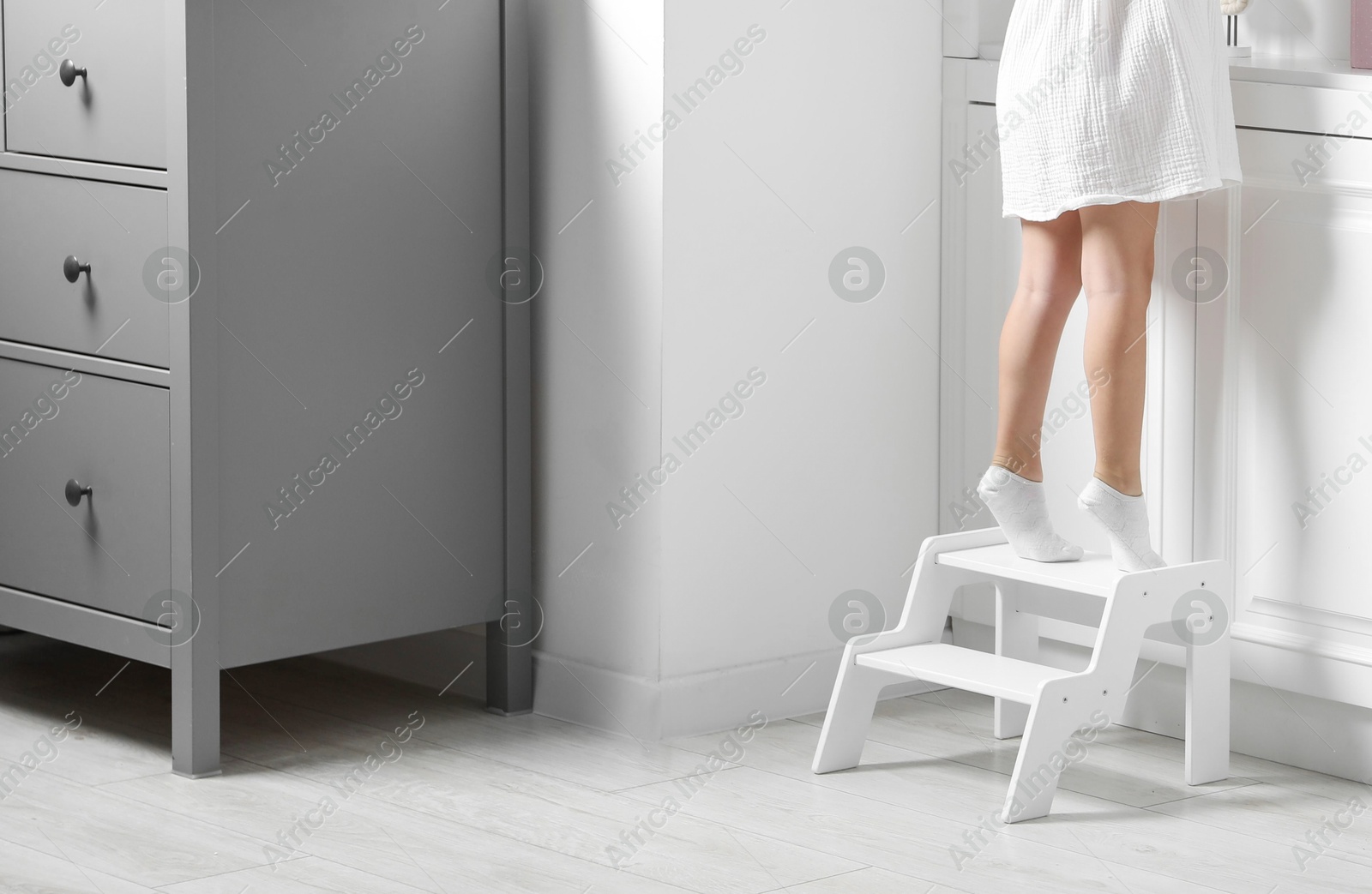 Photo of Little girl standing on step stool indoors, closeup. Space for text