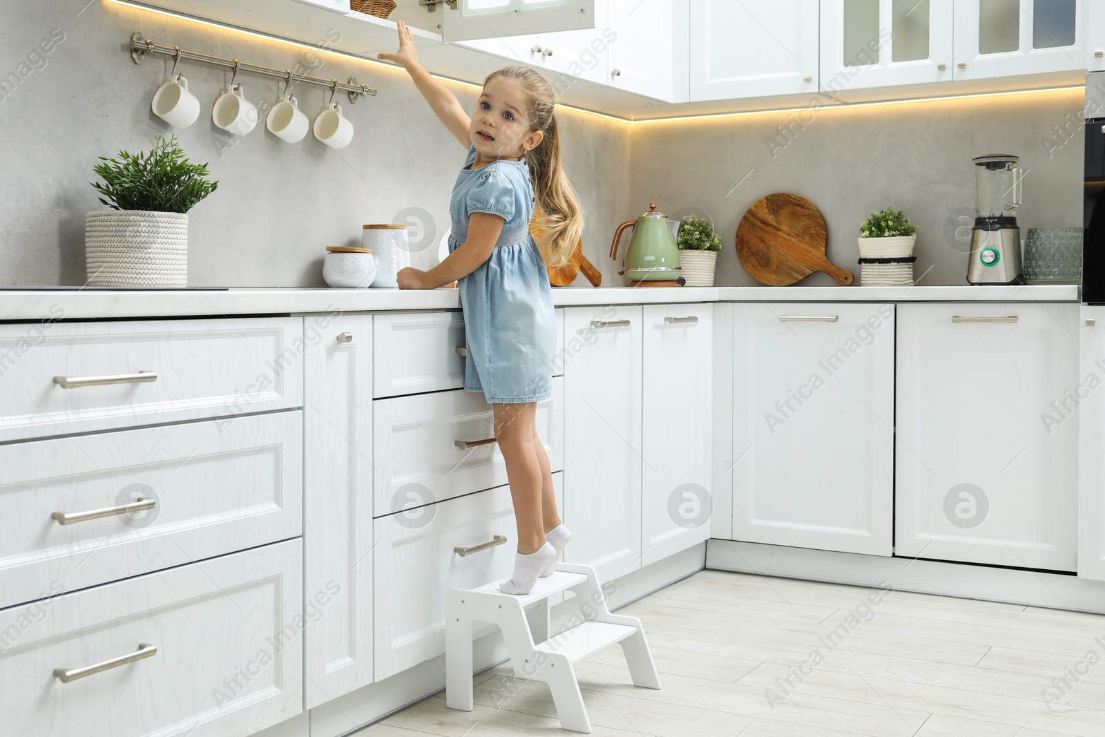 Photo of Little girl standing on step stool and reaching towards counter in kitchen