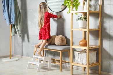 Photo of Little girl standing on step stool at home