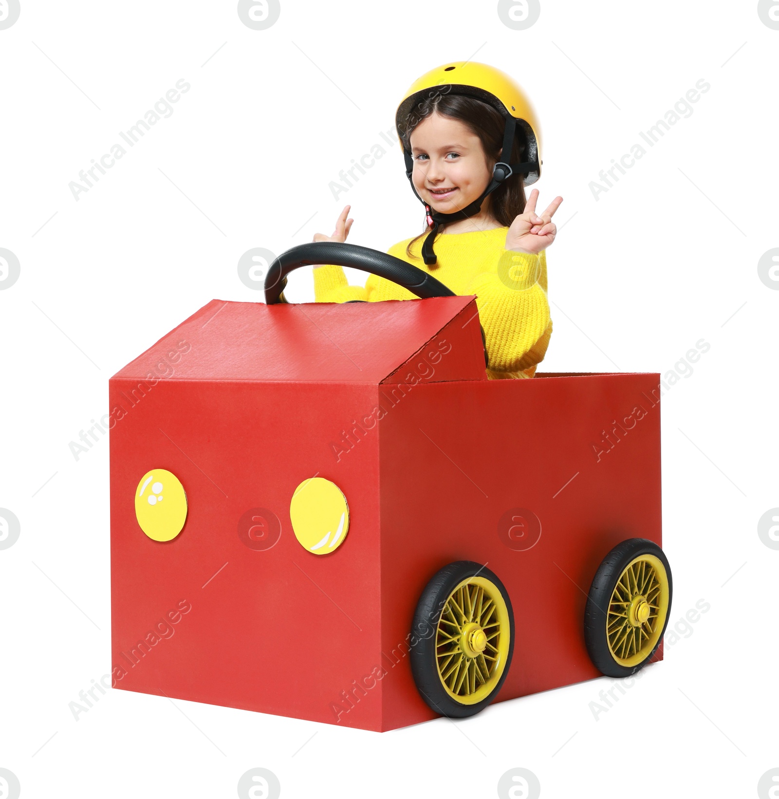 Photo of Little girl showing V-sign while driving car made with cardboard on white background