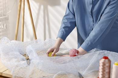 Photo of Woman marking fabric with chalk at table in workshop, closeup