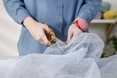 Photo of Woman cutting tulle fabric at table in workshop, closeup